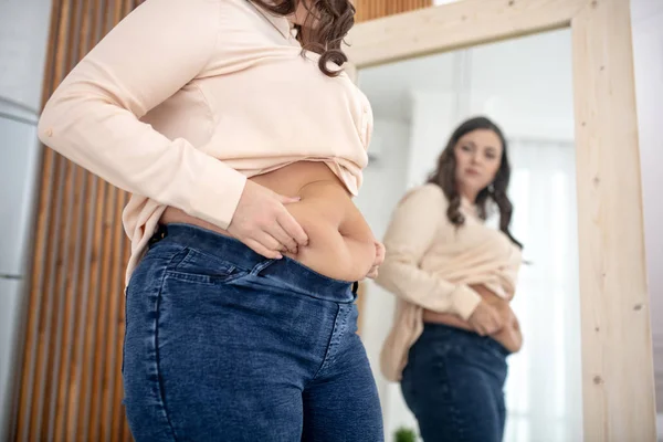 Jovem mulher em uma blusa bege examinando seus abdominais — Fotografia de Stock