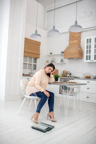 Young woman in a beige blouse sitting and feeling sad — Stockfoto