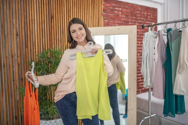 Young woman in a beige blouse choosing a new tshirt — Φωτογραφία Αρχείου