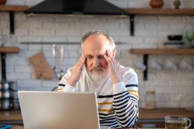 Gri saçlı sakallı son sınıf öğrencisi kafasına dokunuyor.