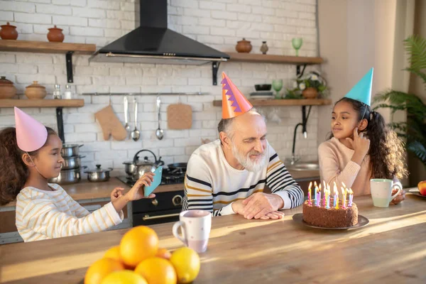 Homme barbu dans un chapeau d'anniversaire célébrant son anniversaire avec ses petites-filles — Photo