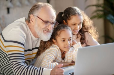 Gri saçlı sakallı adam torunlarıyla vakit geçiriyor.