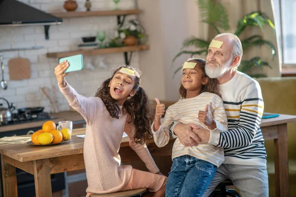 Grijsharige man met baard en zijn kleindochters zien er vrolijk uit — Stockfoto