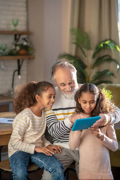 Hombre barbudo de pelo gris y sus nietas viendo un video juntos y sonriendo — Foto de Stock