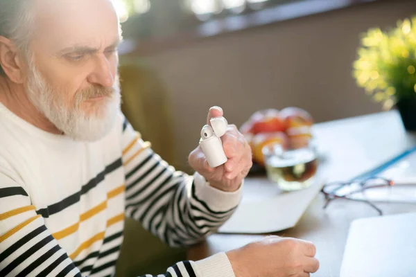 Старший чоловік в смугастому светрі тримає бездротові навушники — стокове фото