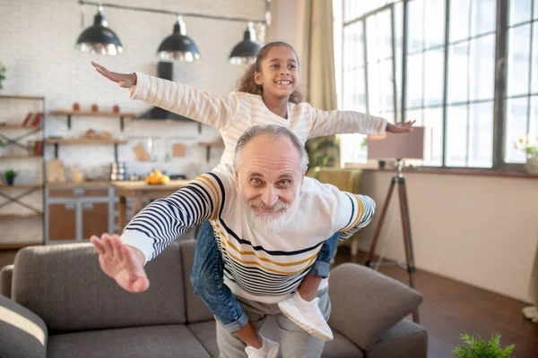 Skäggig gråhårig man som roar sig med sitt mörkhyade barnbarn — Stockfoto