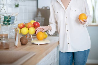 Masanın yanında duran bir kadının ellerinde turuncu.