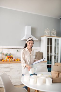 Masanın yanında elinde defter ve kutu olan genç bir kadın..