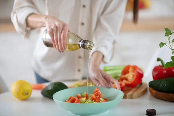 Manos de una joven que vierte aceite de oliva en una ensalada . — Foto de Stock