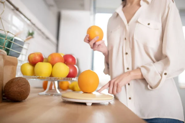 Γυναίκα σε μπεζ μπλούζα στέκεται κοντά στο τραπέζι με φρούτα. — Φωτογραφία Αρχείου