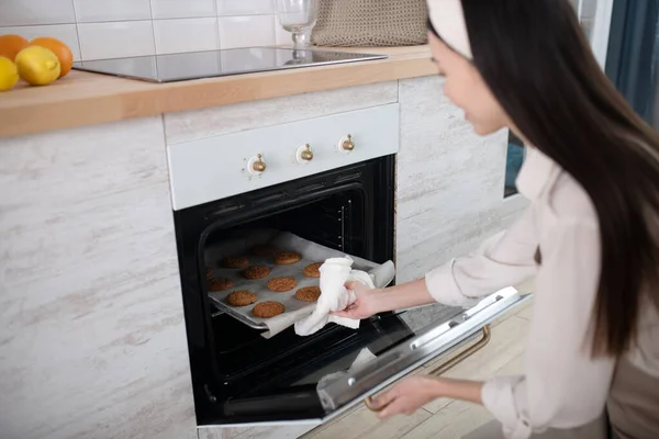 Jeune femme assise près du four avec plaque à pâtisserie à la main . — Photo