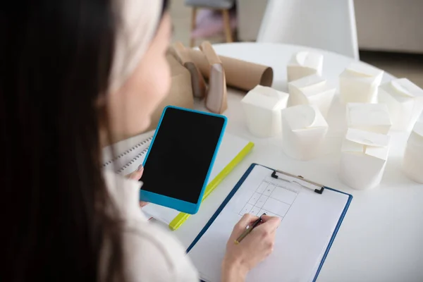 Mujer dibujando una mesa en un cuaderno sentado a la mesa . — Foto de Stock