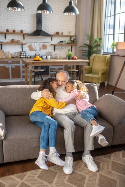 Twee meisjes knuffelen hun grootvader gevoel comfortabel — Stockfoto