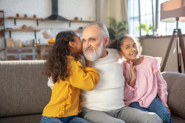 Милая длинноволосая девушка говорит что-то на ухо своему дедушке — стоковое фото