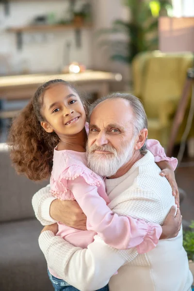 Седовласый мужчина обнимает свою милую внучку и выглядит счастливым — стоковое фото