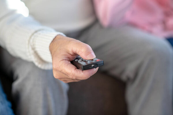 Крупный план человека, сидящего на диване с дистанционным управлением в руке
