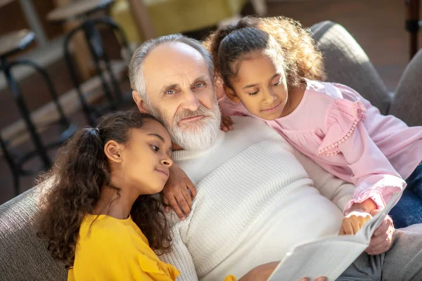 Abuelo canoso leyendo un libro a sus nietas —  Fotos de Stock