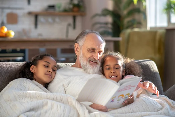 Grijsharige opa die verhaaltjes voorleest aan zijn kleindochters — Stockfoto