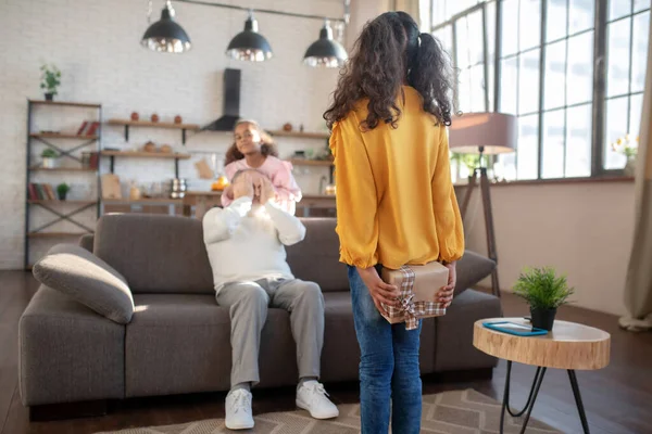 Fille mignonne à la peau foncée cachant un cadeau pour son grand-père — Photo