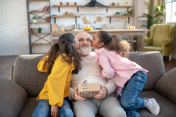 Duas irmãs de pele escura beijando seu avô e dando presente bday hime — Fotografia de Stock