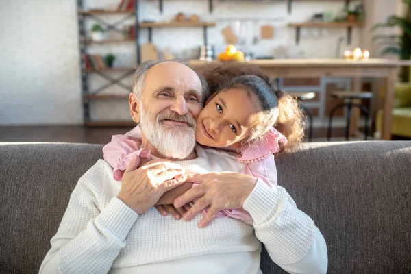 Ragazza dalla pelle scura con i capelli ricci che abbracciano il nonno e sembrano pacifici — Foto Stock