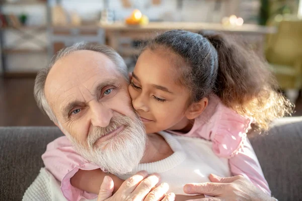 Fille à la peau foncée avec les cheveux bouclés étreignant son grand-père et se sentant paisible — Photo