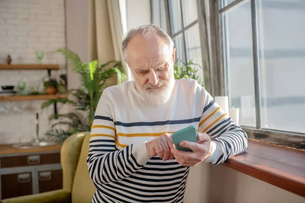 Homem de cabelos grisalhos barbudo em uma camisola listrada digitando uma mensagem — Fotografia de Stock