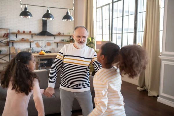 Skäggig man i randig tröja dansar med två mörkhyade tjejer som håller sina händer — Stockfoto