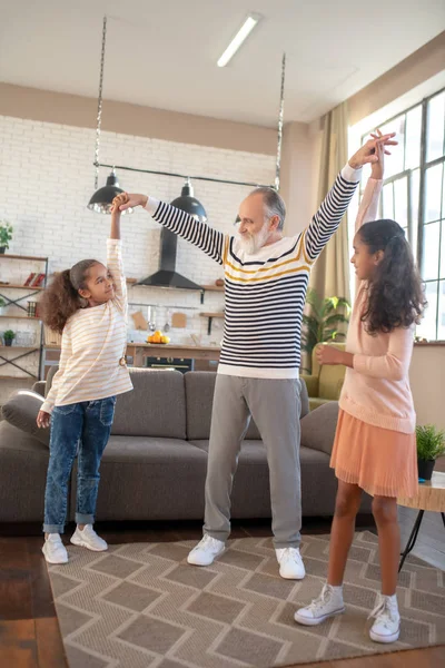 Skäggig gråhårig man dansar med sina barnbarn och mår bra — Stockfoto