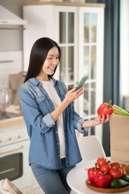 Akıllı telefonu ve kırmızı biberi olan genç bir kız..