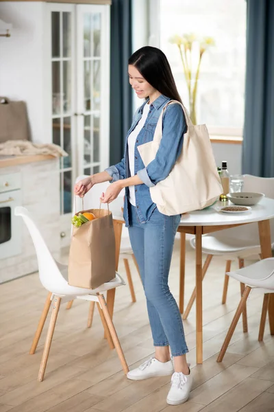 Young woman standing in the kitchen putting bag on chair. — Stock Photo, Image