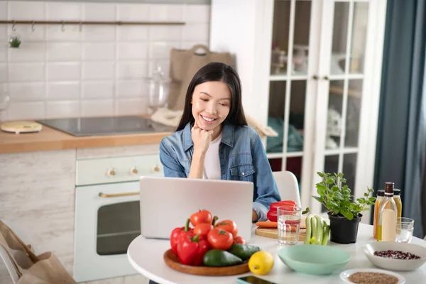 Mujer joven sentada en un portátil en la cocina . — Foto de Stock