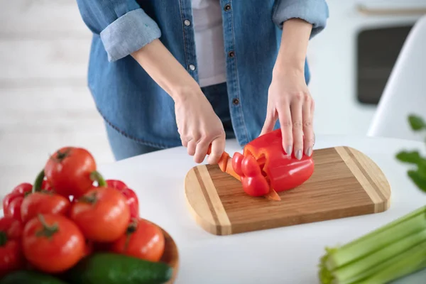 Female hands with knife cutting slice of red pepper. — Stock Photo, Image