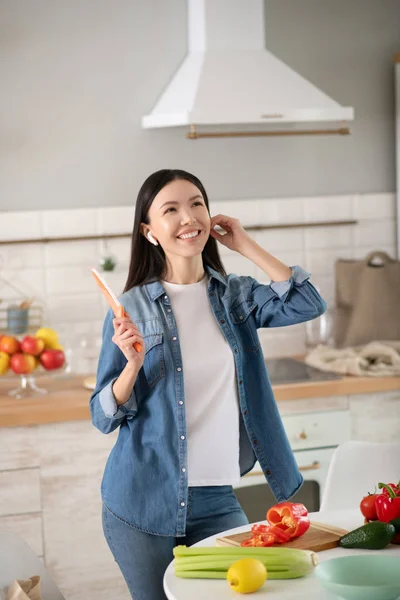 Χαρούμενη νεαρή γυναίκα με ασύρματα ακουστικά μαγειρεύοντας μια σαλάτα. — Φωτογραφία Αρχείου