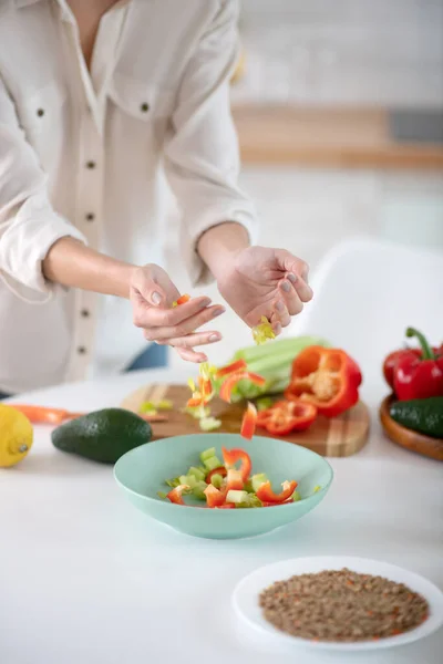Γυναικεία χέρια ρίχνουν τεμαχισμένα λαχανικά σε ένα πιάτο. — Φωτογραφία Αρχείου