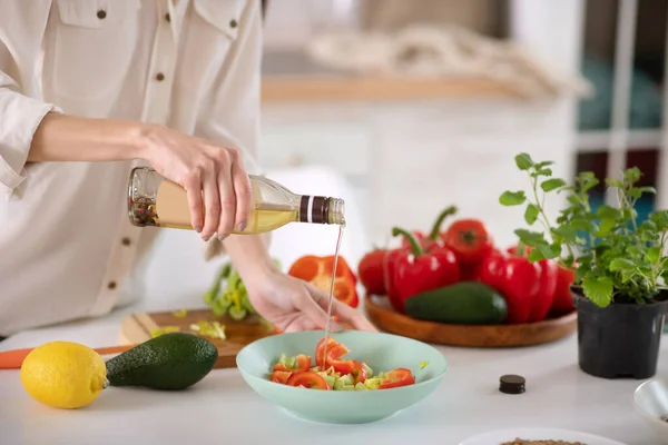 Manos femeninas sosteniendo una botella de aceite vegetal sobre un plato . — Foto de Stock