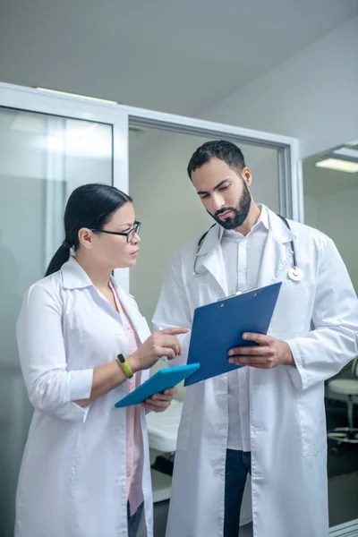 Dark-haired male and female doctors standing in the room together discussing results — Stockfoto