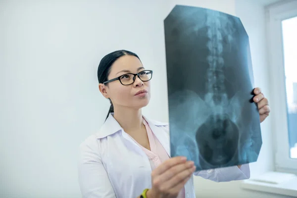 Dark-haired female doctor analyzing xray results of backbones — Stock Photo, Image