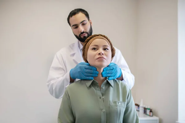 Male doctor in blue gloves examining neck nodes of his female patient