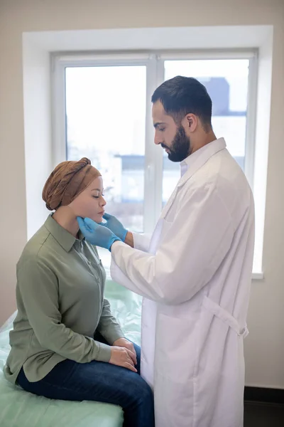 Tall doctor in blue gloves palping lymph nodes of female patient — Stockfoto