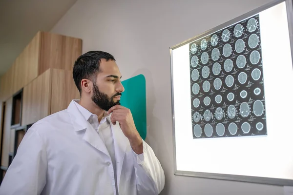 Bearded young doctor looking thoughtful while analyzing MRI results — ストック写真