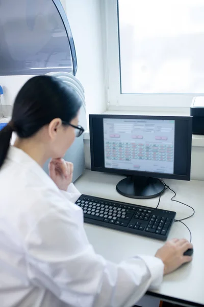 Dark-haired doctor in a white robe working on a computer looking thoughtful — Φωτογραφία Αρχείου