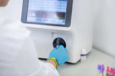 Technician in blue gloves pressing the start button of hematological analyzer in laboratory