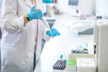 Technician in blue gloves pouring blood sample into the test tube in the laboratory