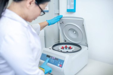 Technician in blue gloves closing the cover of centrifuge