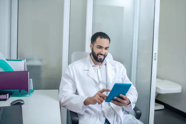 Male doctor in a white robe reading something on internet — Φωτογραφία Αρχείου