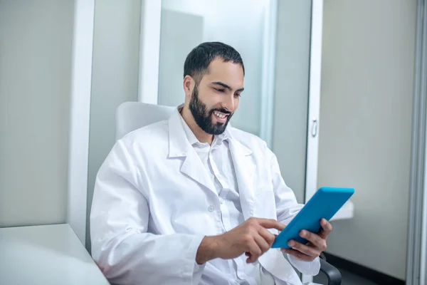 Male doctor in a white robe reading something and smiling — 图库照片