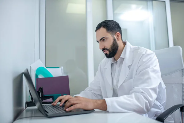 Male doctor in a white robe typing a message — Stock fotografie