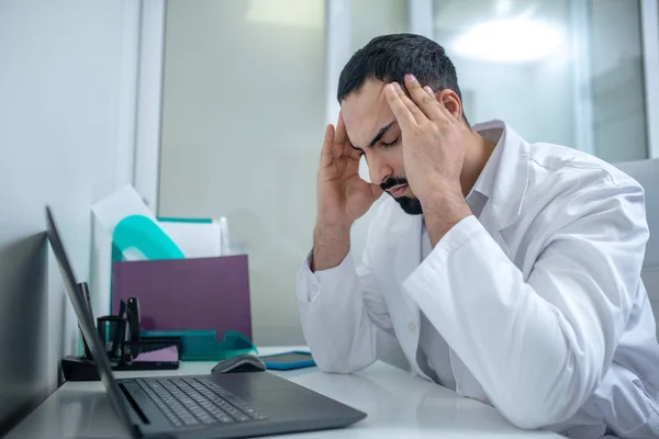 Male doctor in a white robe having a headache — Stockfoto