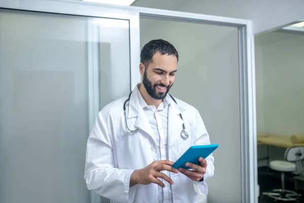 Мужчина-врач в белом халате ищет в интернете и улыбается — стоковое фото